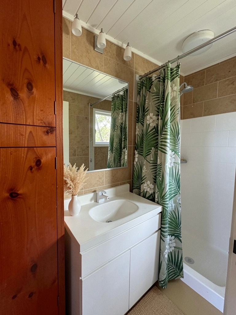 Banheiro com box de vidro e cortina estampada com folhagens tropicais, ganchos metálicos modernos