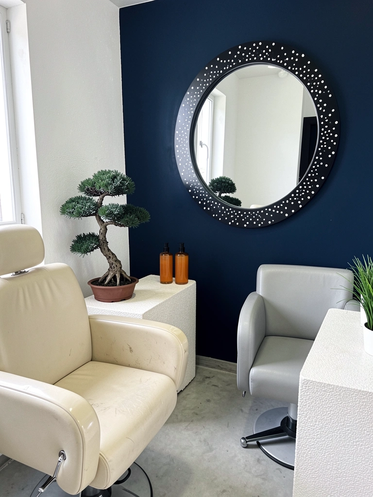 Parede azul escura em sala pequena com sofá claro, mesa de centro de madeira e espelho redondo ampliando o espaço